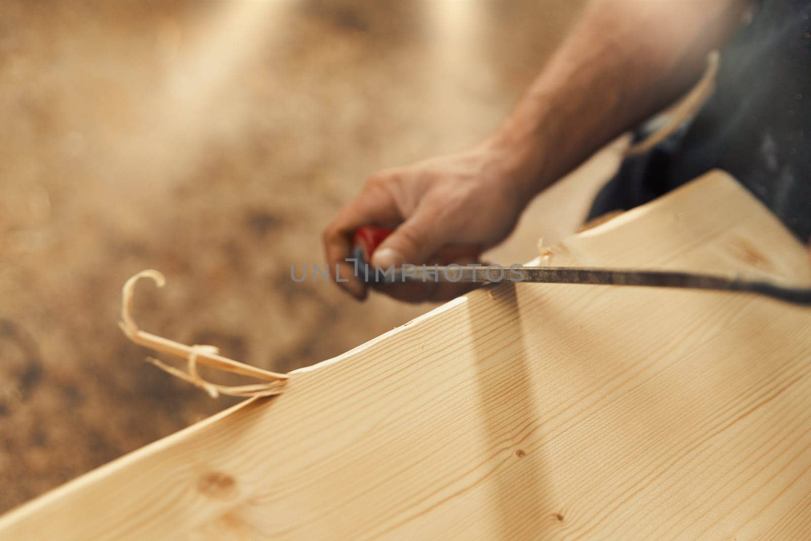 The artisan carves and chamfers the edges of the wooden boards that make up the furniture with a drawknife. Strong male hands and wood are visible, embodying the essence of carpentry
