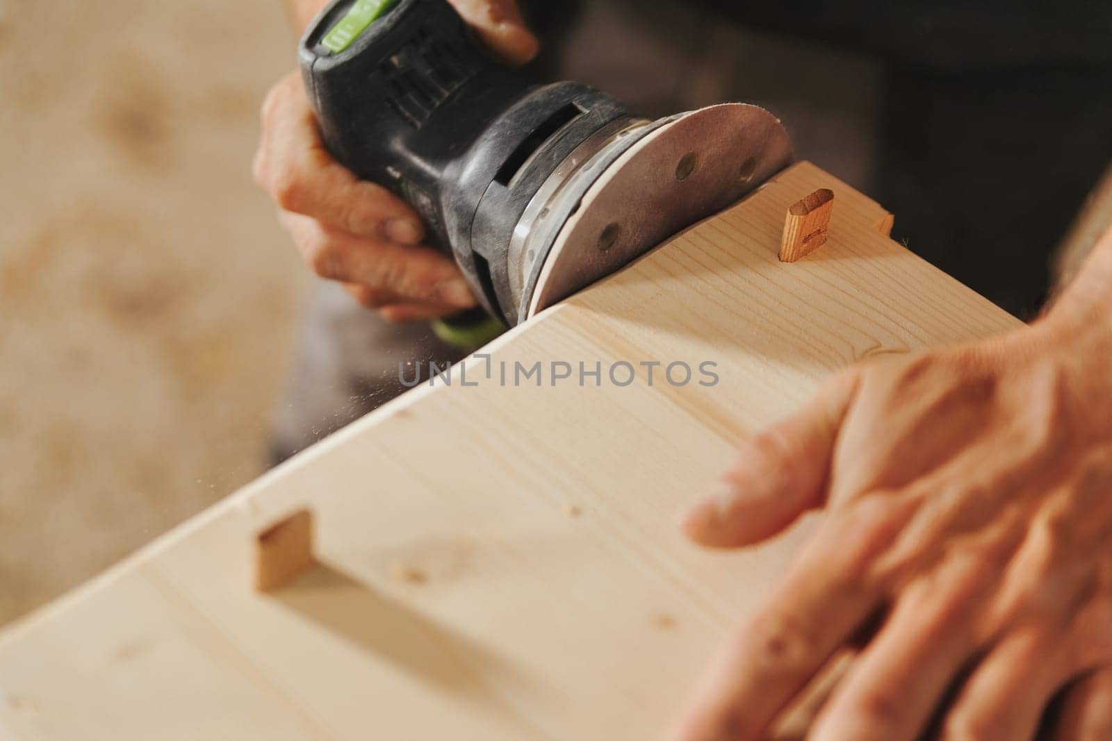Carpenter at work with a modern sander. A small tool that moves sandpaper at high speed with the precision and control the craftsman wishes to impart. Details of hands at work and the wood.
