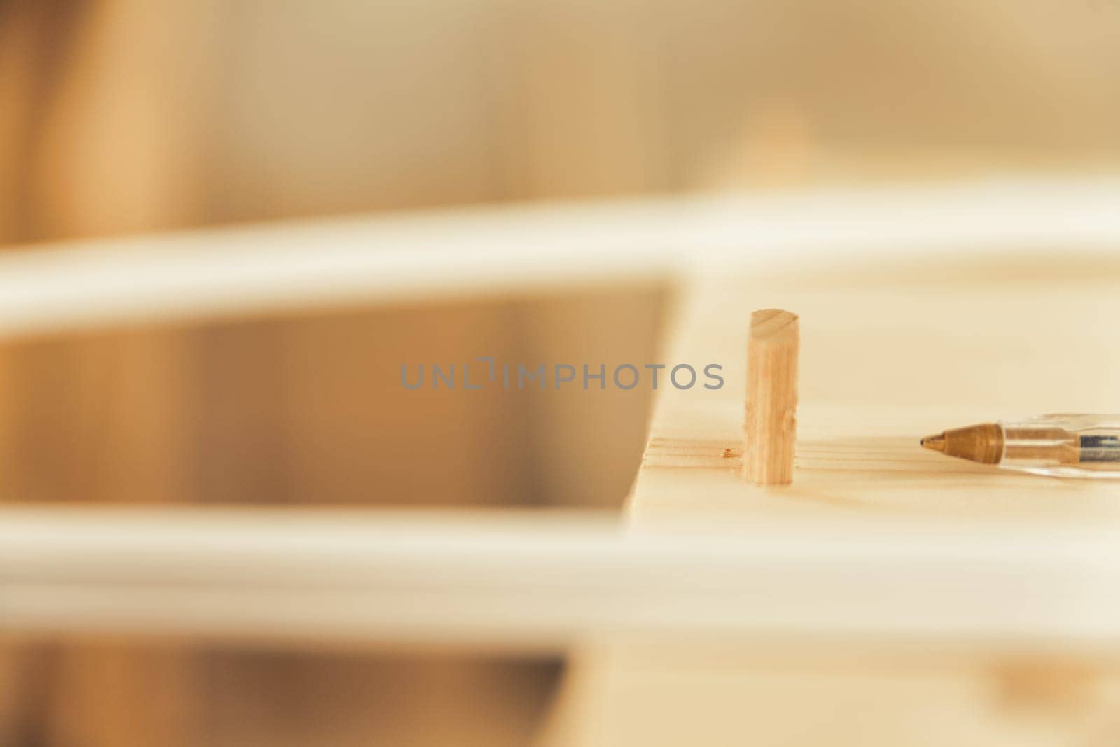 Pen tip near working wood. In focus is only the dowel ready to fasten various parts of a piece of furniture and the tip of a cheap but excellent ballpoint pen.