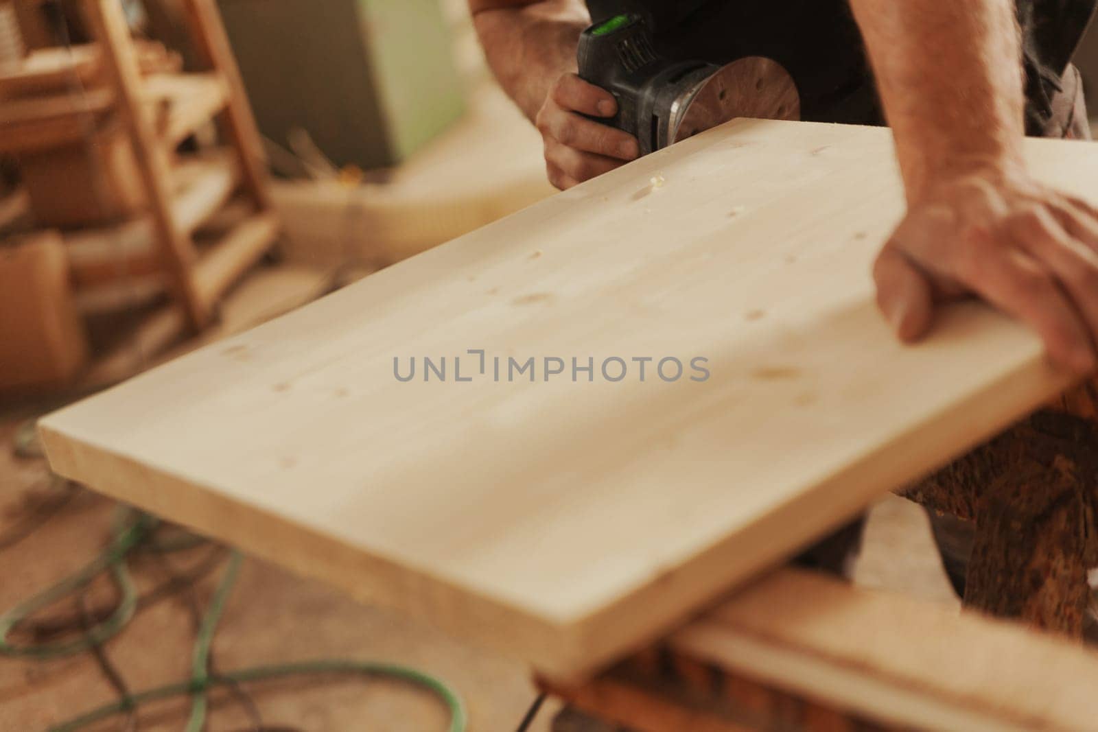Carpenter at work with a modern sander. A small tool that moves sandpaper at high speed with the precision and control the craftsman wishes to impart. Details of hands at work and the wood.