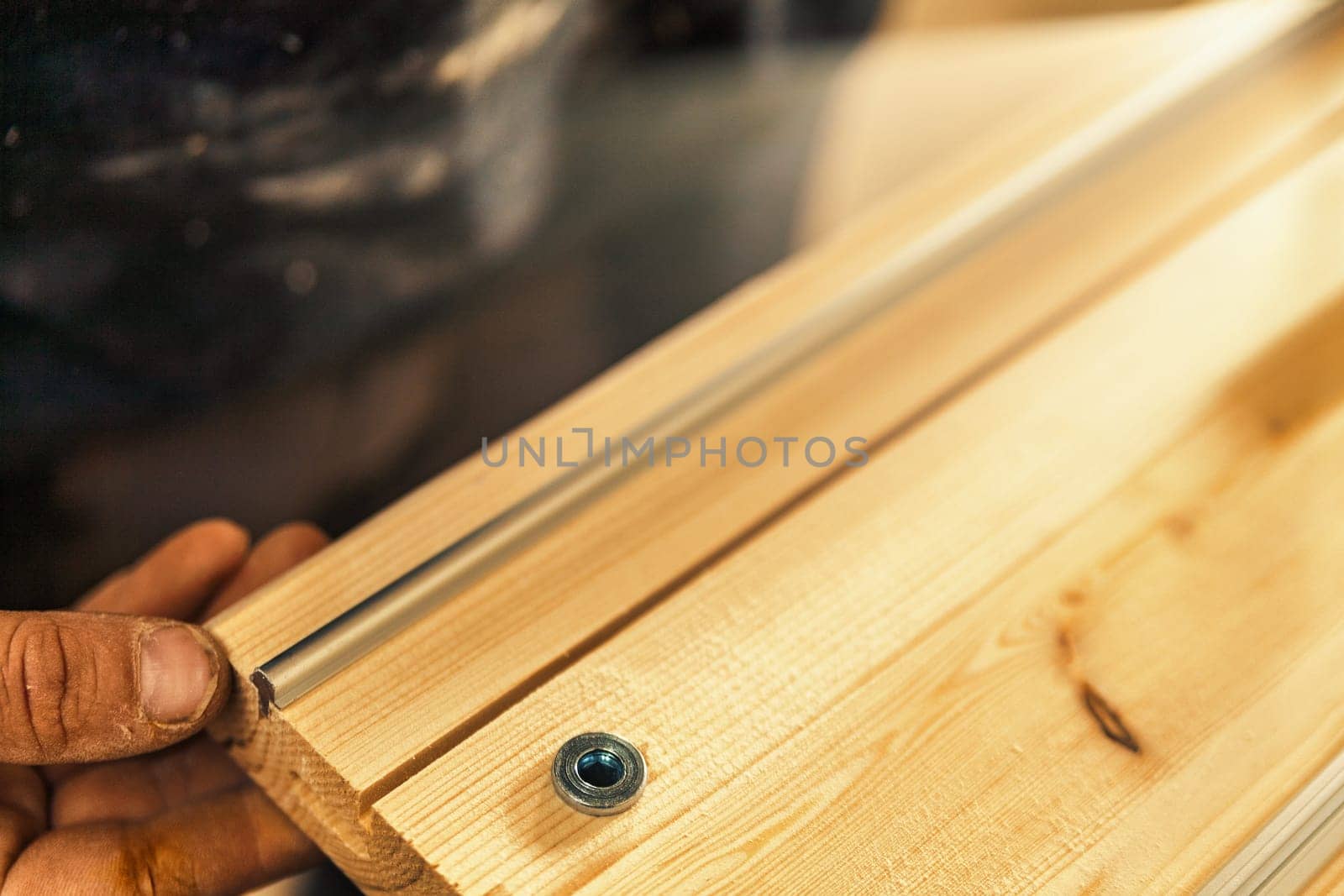 A metal detail in the lower left corner takes up a small part of the shot, while the rest of the frame is filled with blurred wooden elements. The presence of the carpenter is hinted at but barely vis