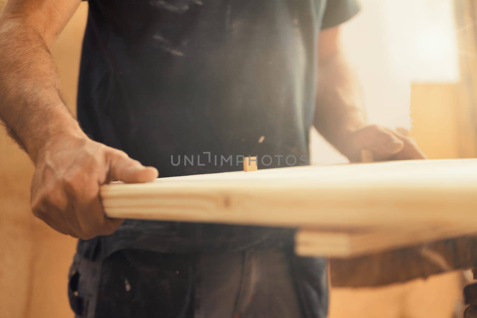 Strong carpenter's hands hold, guide, restrain, push, and move lumber while working with powerful cutting machines in his workshop. Image conveys strength, skill, and risk-taking expertise