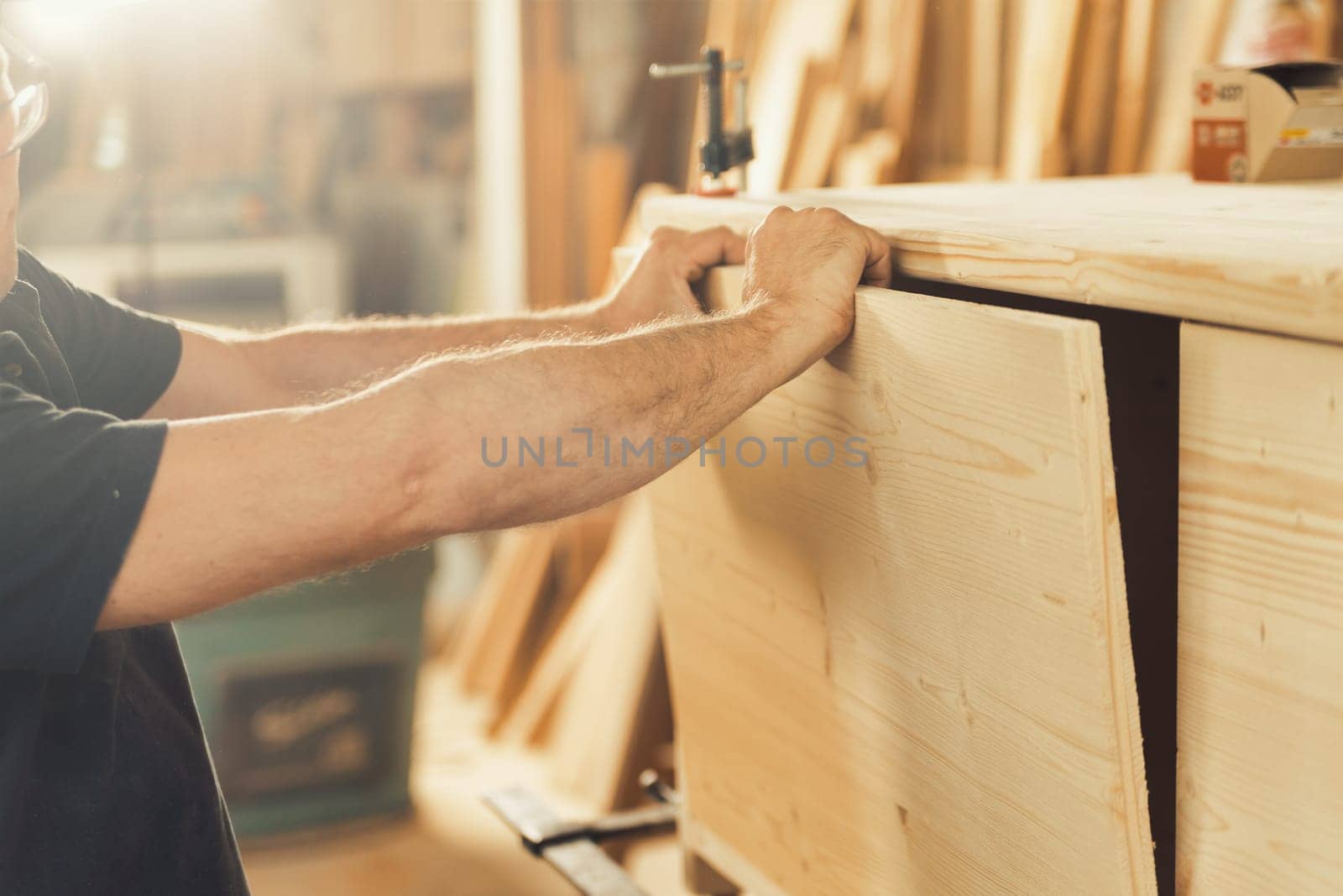 Strong carpenter's hands hold, guide, restrain, push, and move lumber while working with powerful cutting machines in his workshop. Image conveys strength, skill, and risk-taking expertise