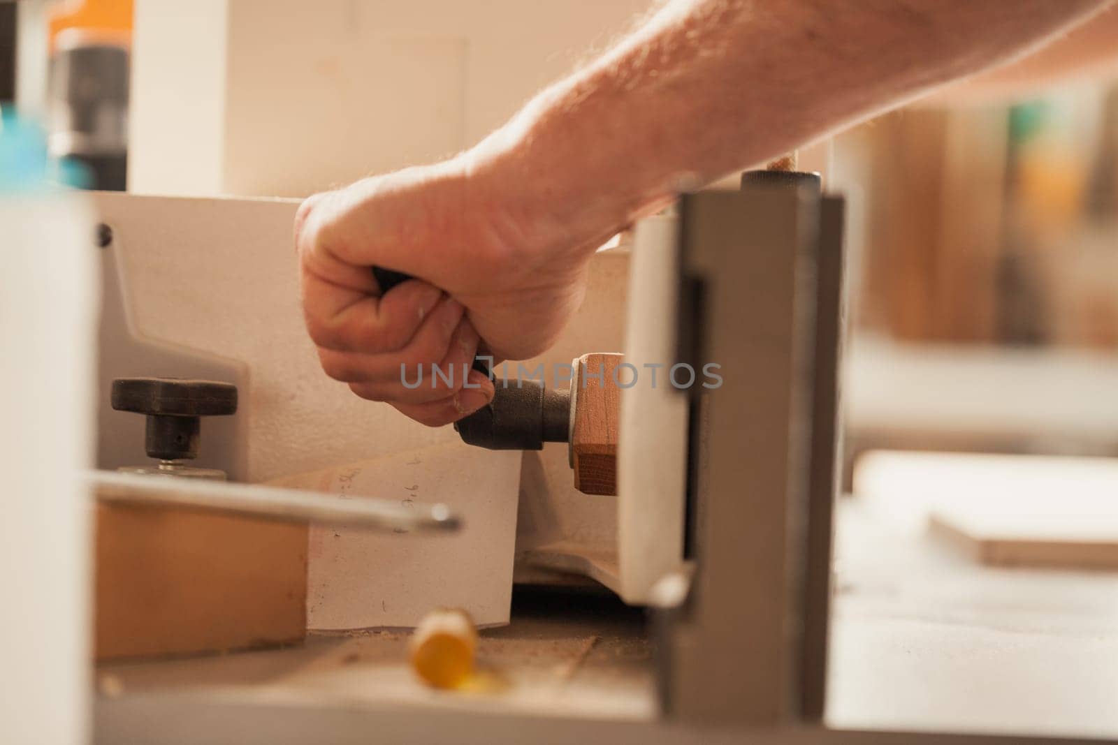 The carpenter's hand grips a self-made vise using a lever. Visible is his hand and the piece, while the arm and everything else is blurred.