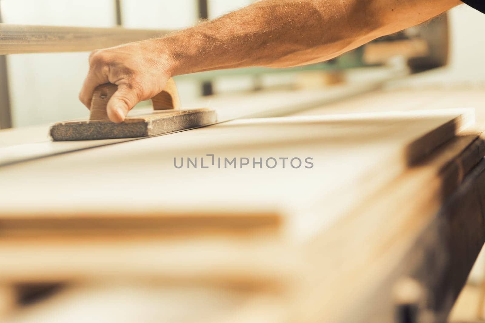 The professional woodworker uses a modern planer or sander with a manual component. He works with ease but applies effort where necessary, shown here smoothing long planks on a large machine