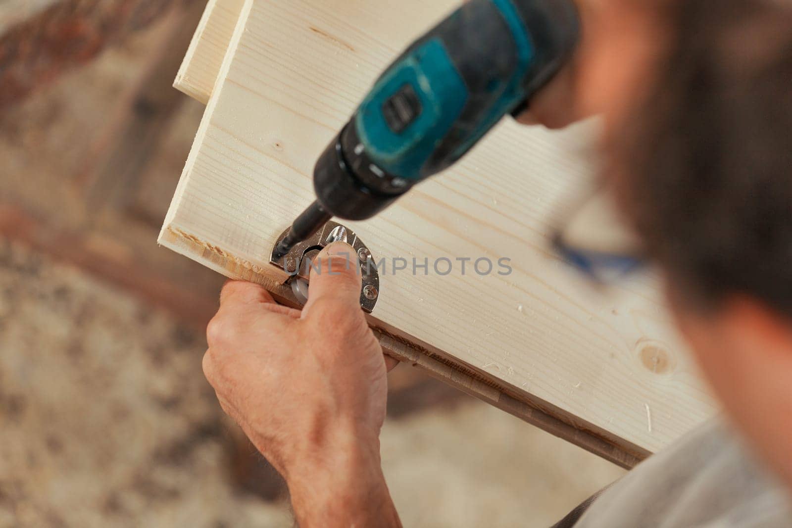Detail in focus on the action of screwing a hinge onto a handcrafted piece of furniture produced by a carpenter. Strong hands and arms of the craftsman in view and lots of light wood.