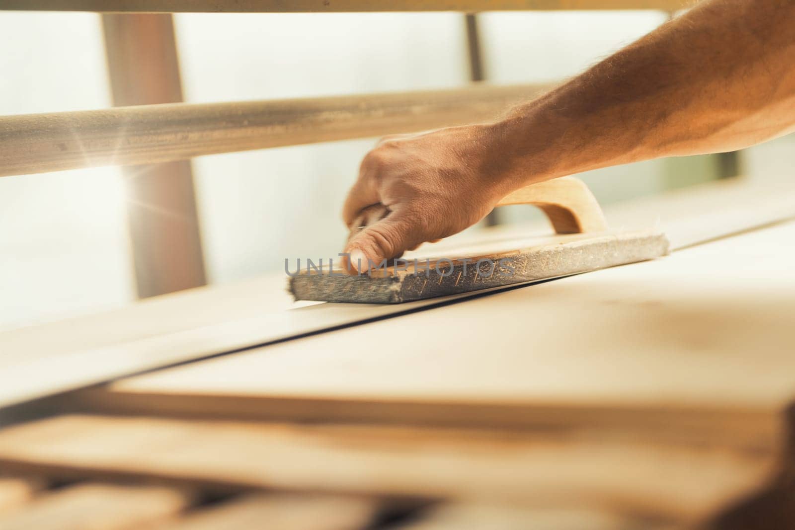 The professional woodworker uses a modern planer or sander with a manual component. He works with ease but applies effort where necessary, shown here smoothing long planks on a large machine
