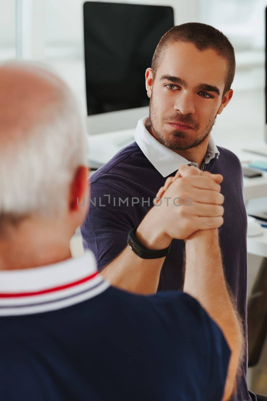 Young man in a navy polo exudes confidence during an arm-wrestled handshake with an elder on the job