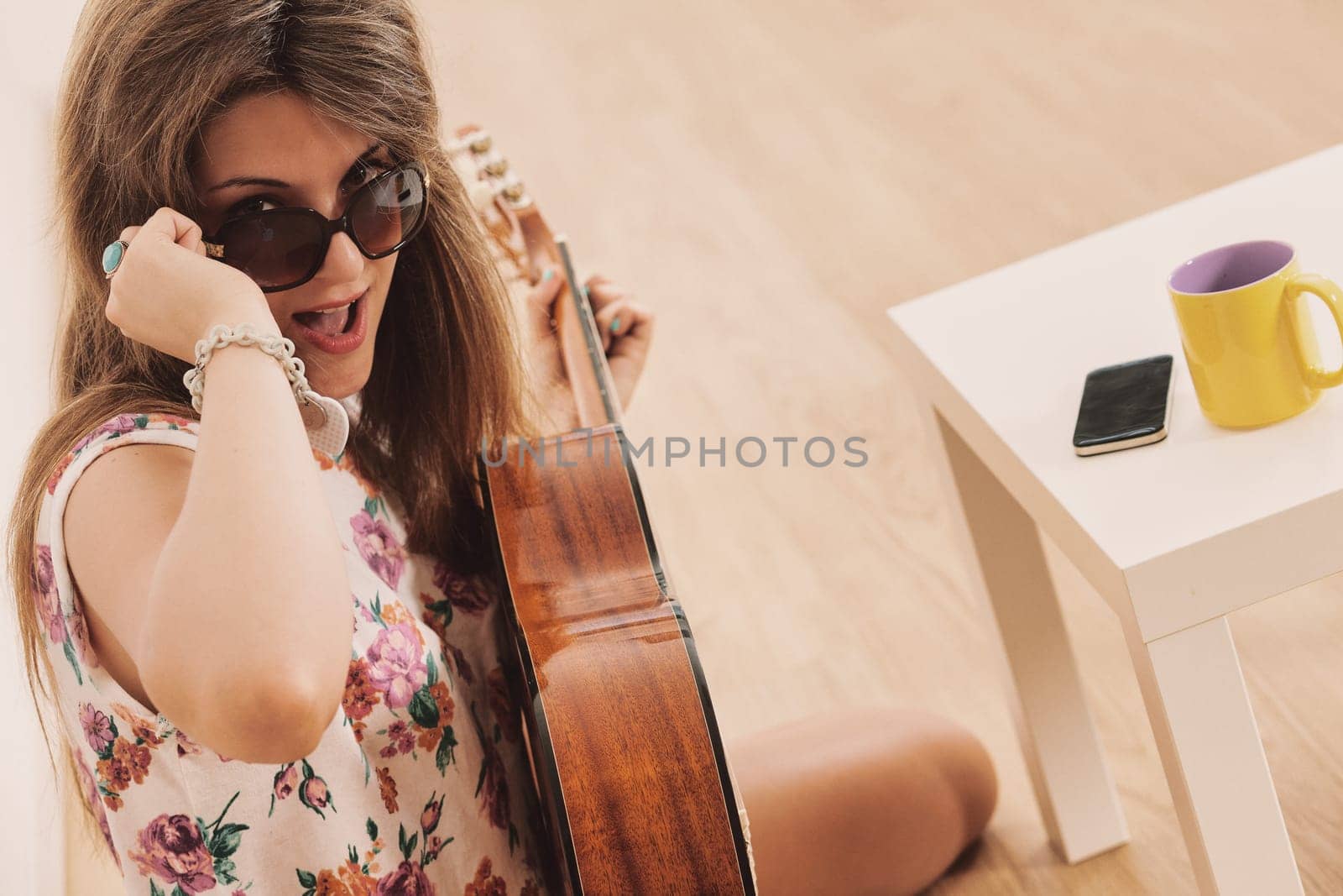Girl with sunglasses used to be a fashionable chick, at a party or in her room plays or pretends to play classical guitar like a pop star.