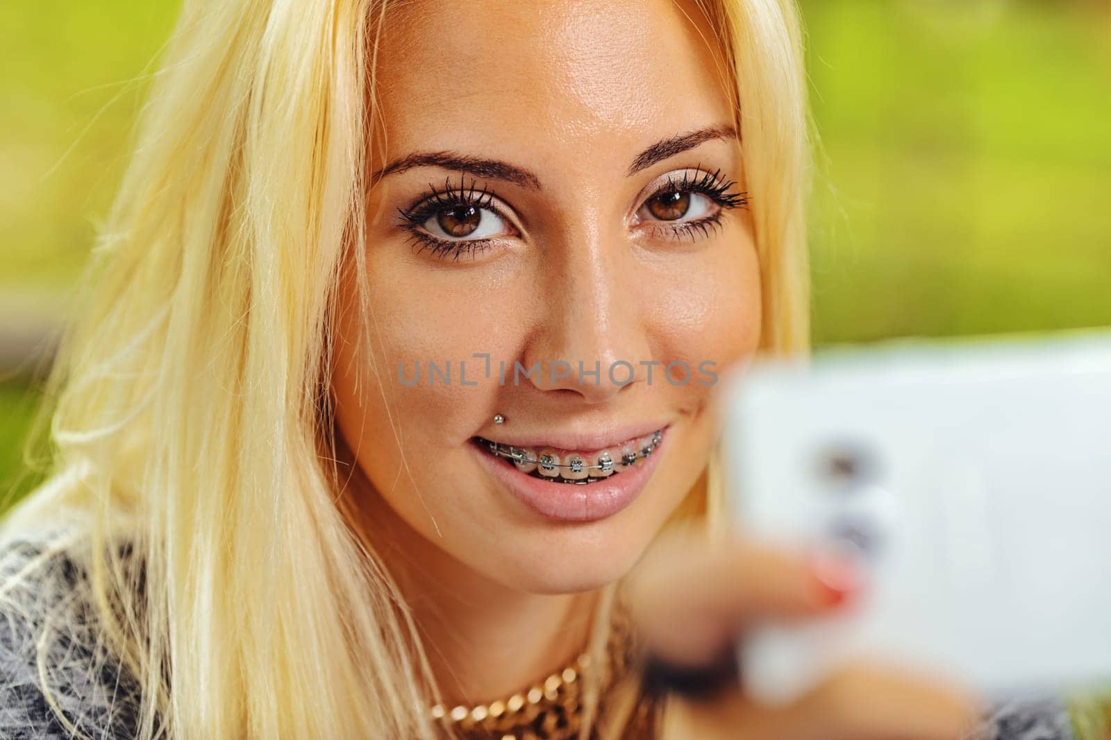 Interlocutory look of beautiful smiling girl with braces. She turns her sight away from her smartphone (blurred in the foreground) to turn it to us.