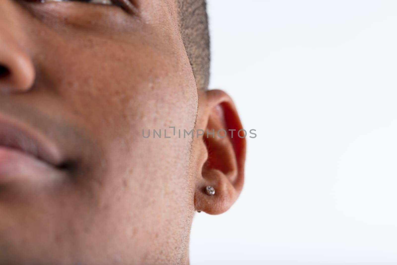 'In-focus detail of an earring on a young black man's ear. Barely anything else visible but a hint of a smile, all blurred. Rest is white background
