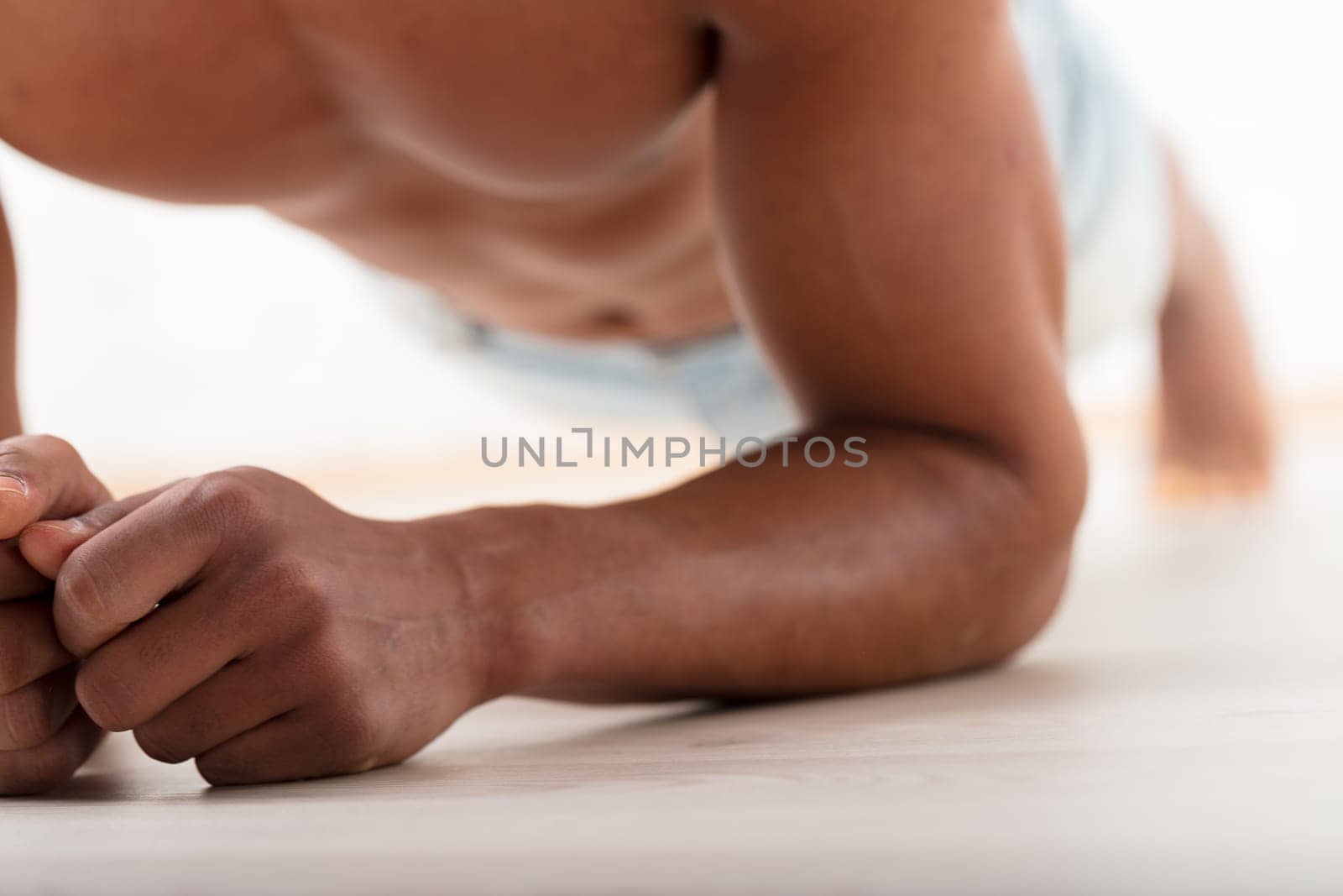 Unrecognizable black man holds a stoic plank, elbows grounded. His evident pectorals and abs show his commitment to exercise for attractiveness and long-term health