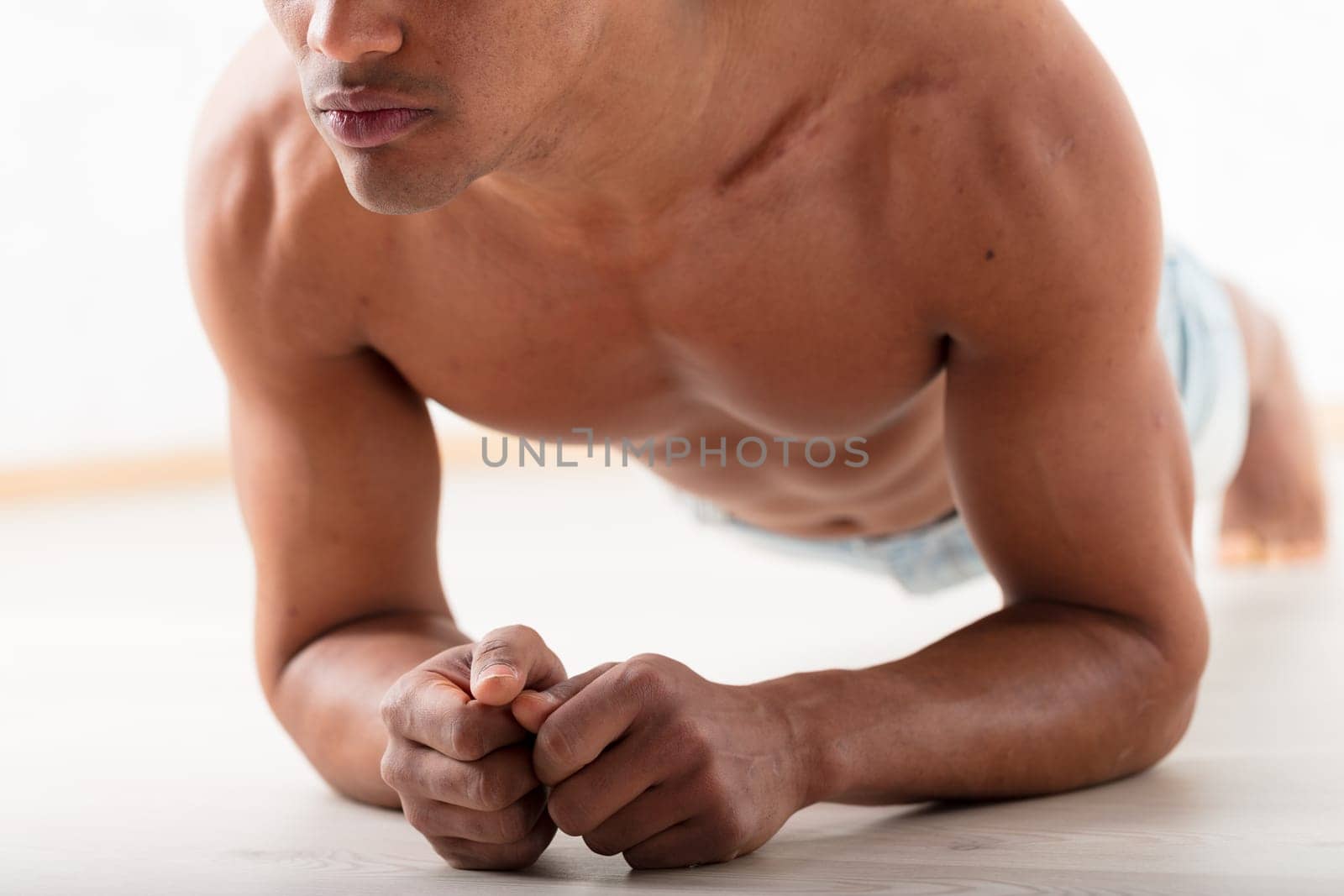 An unidentifiable black man performs a plank with his elbows on the ground. His noticeable pecs and abs prove that exercise enhances appeal and health