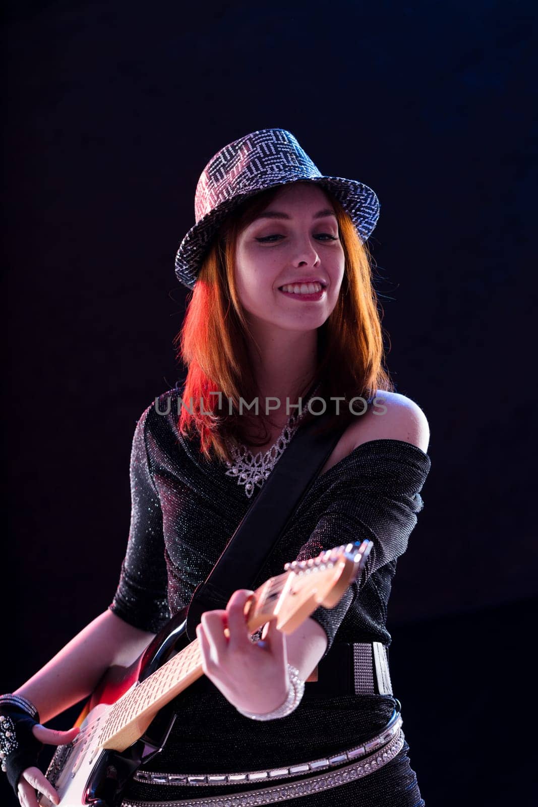 Radiant female guitarist with red hair strums her instrument with visible joy in a sparkling outfit