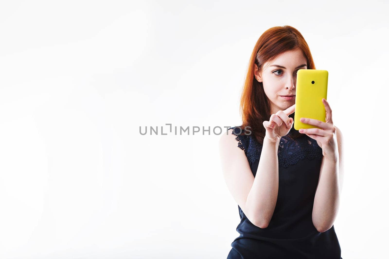 Concentrated and poised, the woman with auburn hair uses her vibrant smartphone, embodying the modern digital experience