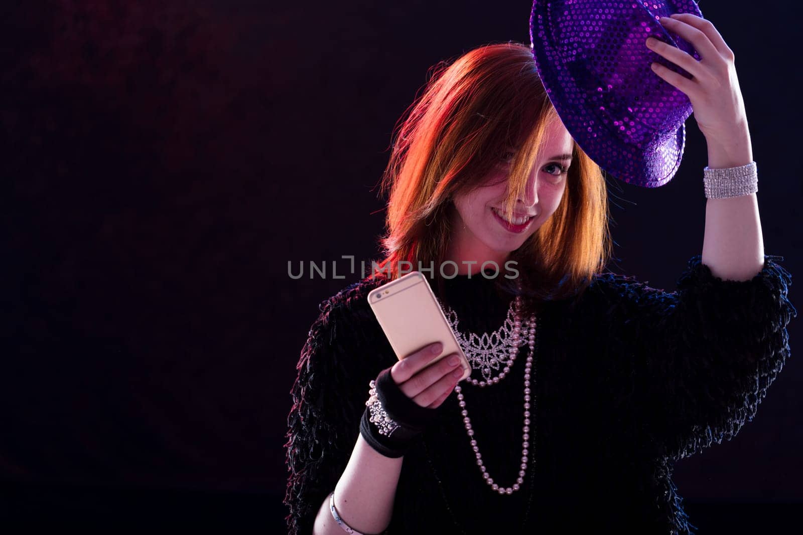 Red-haired woman in a gleaming hat enjoys the limelight, capturing the moment with a self-portrait