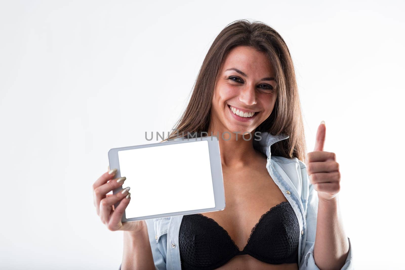 Fit woman with a digital tablet for workout and training organization. Open denim shirt reveals flat stomach. Tablet screen left blank for your app, against a white backdrop
