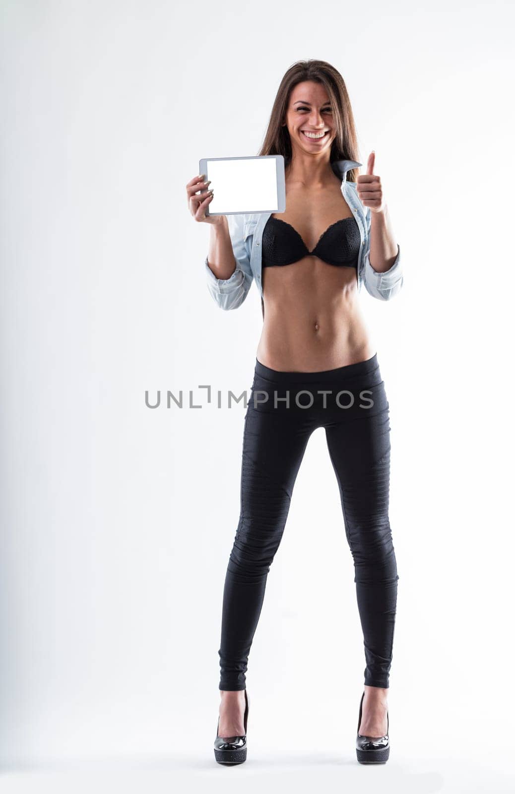 Young woman with a perfect figure, utilizing a digital tablet for her workout plans and exercises. Empty tablet screen on white background for your app copyspace