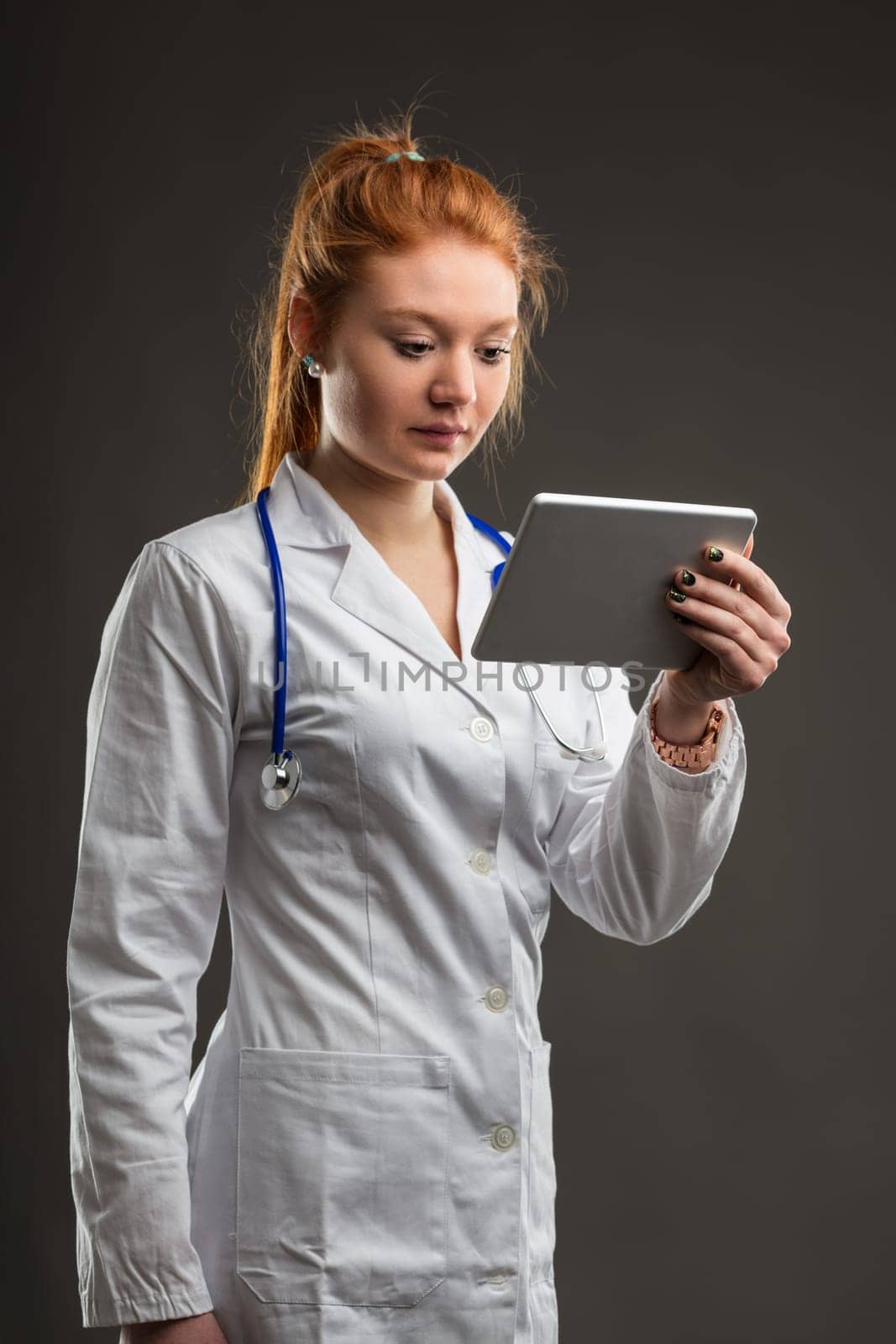 Medical professional consults digital device, her red hair reflecting a unique identity in healthcare