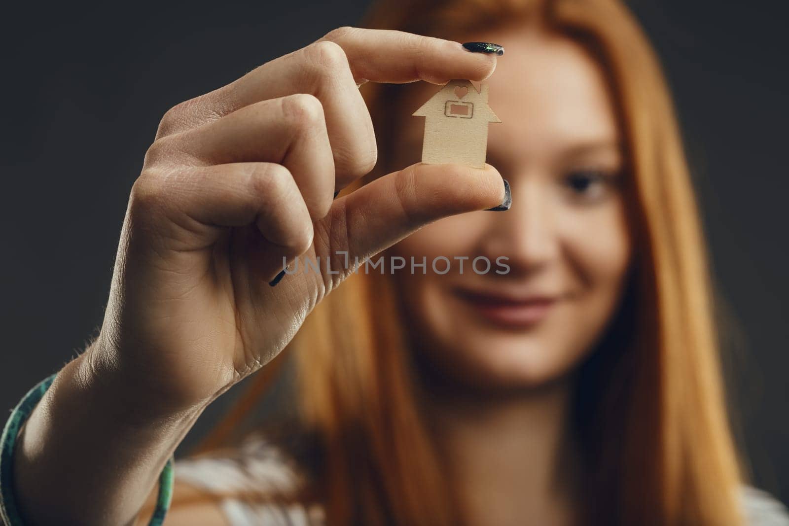Red-haired individual contemplates a tiny house, a symbol of foundation and home