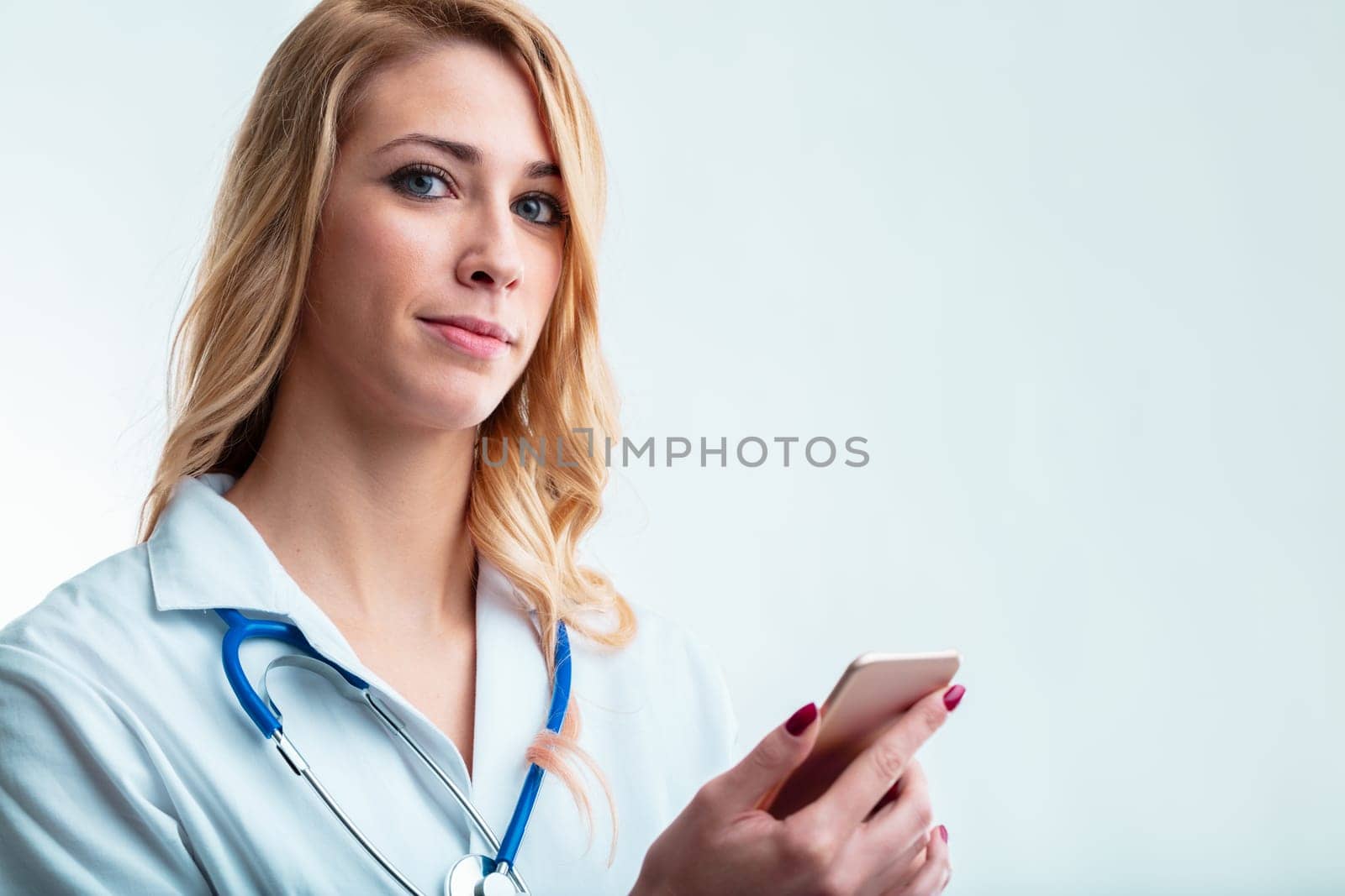 Blonde doctor with mobile device in large copyspace, using medical apps for telehealth, data management, patient records