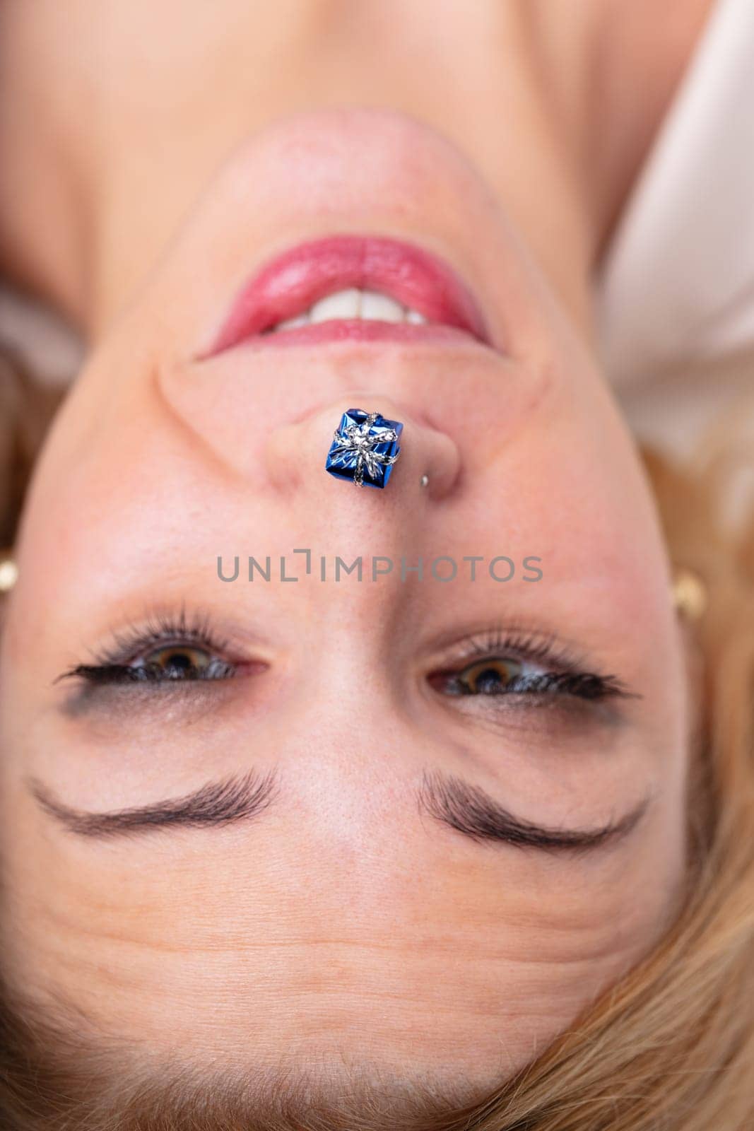 Upside-down face of joyful woman with a tiny gift on her nose. Idea of gifts, Christmas, festivities, celebrations