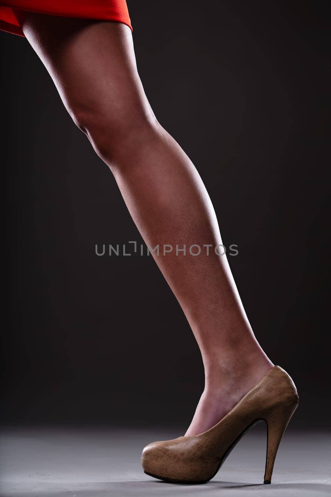 Female leg in action from a red skirt forms a diagonal, highlighted by a moderately high heel, offering classic femininity. Sophisticated grey-black background