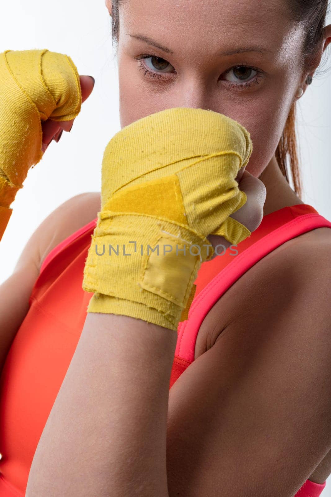 Young woman is a modern, fierce warrior, hands bandaged, in an athletic stance, delivering a punch in an orange top