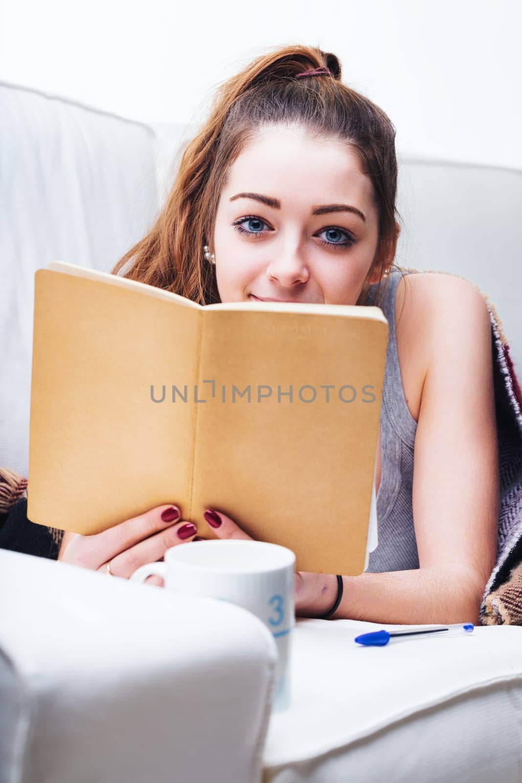 Engrossed in her writing, she lies comfortably on the sofa, her casual attire suggesting a laid-back day at home