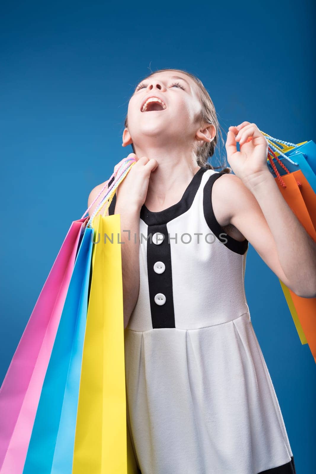 On blue backdrop, girl pretends to be a high-society shopper, pure joy