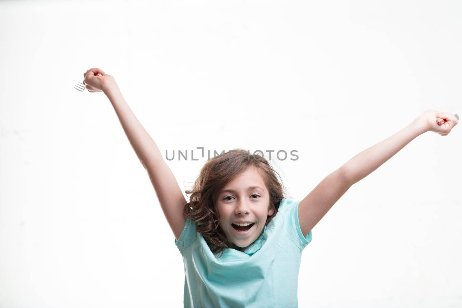 Excited girl in blue, arms up with cutlery, adores mealtime. Her metabolism allows her to indulge without gaining weight