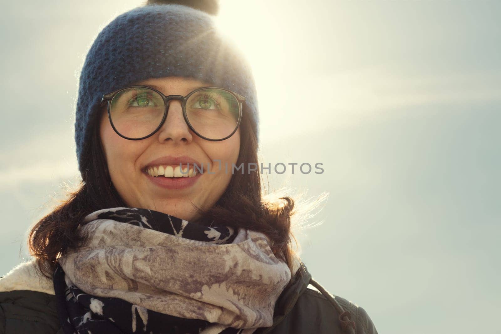 The sun's glare adds a dreamy quality to the woman's blissful smile, wrapped in winter fashion
