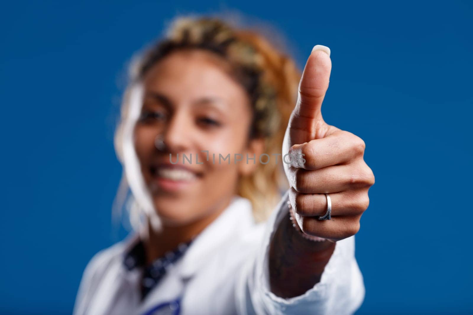 Focus on thumbs-up with manicured nails of competent brown-skinned doctor, who's smiling, approving, reassuring. Keep going with the care!