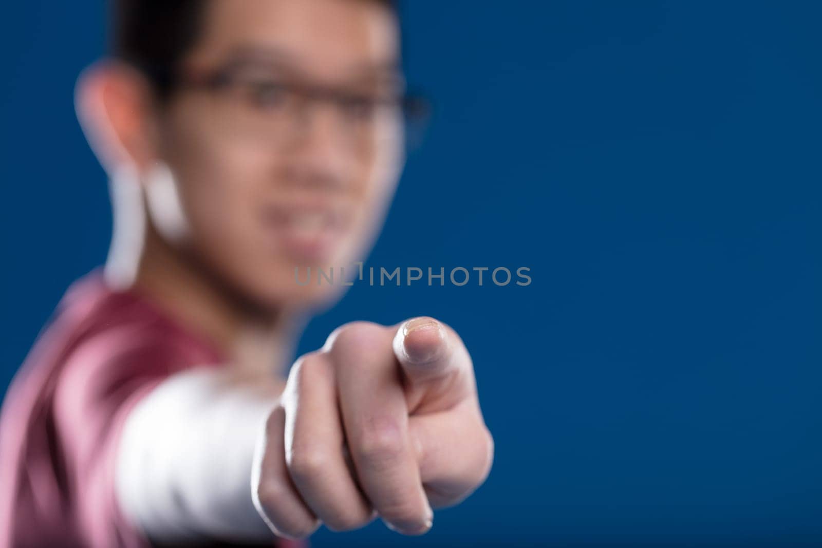Fingertip on a transparent screen in sharp focus, blurry Asian man with glasses in the backdrop on blue. Ideal for touch graphic applications