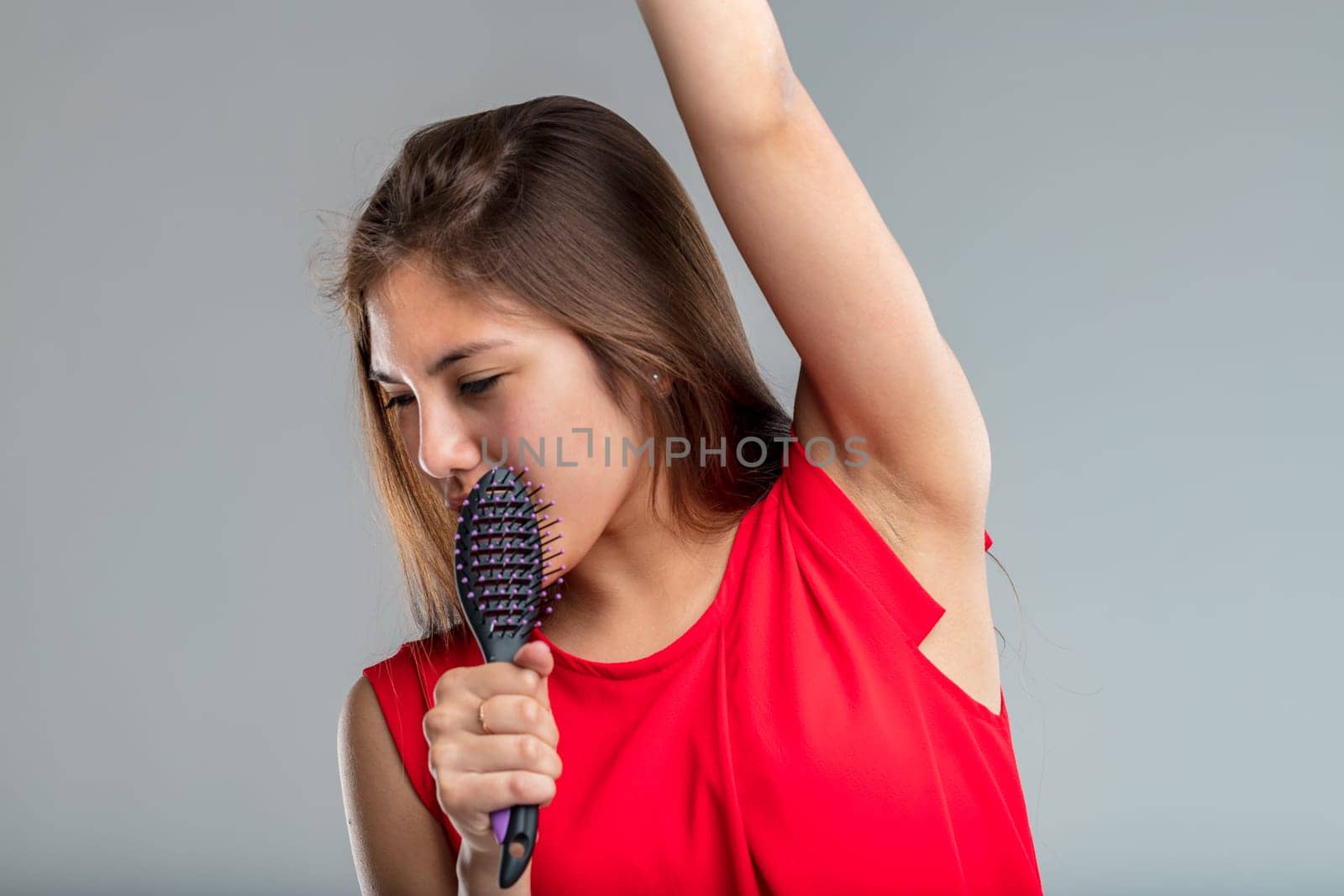 Young woman in red dress sings passionately pretending her hairbrush is a microphone, she is very much into the part and happy