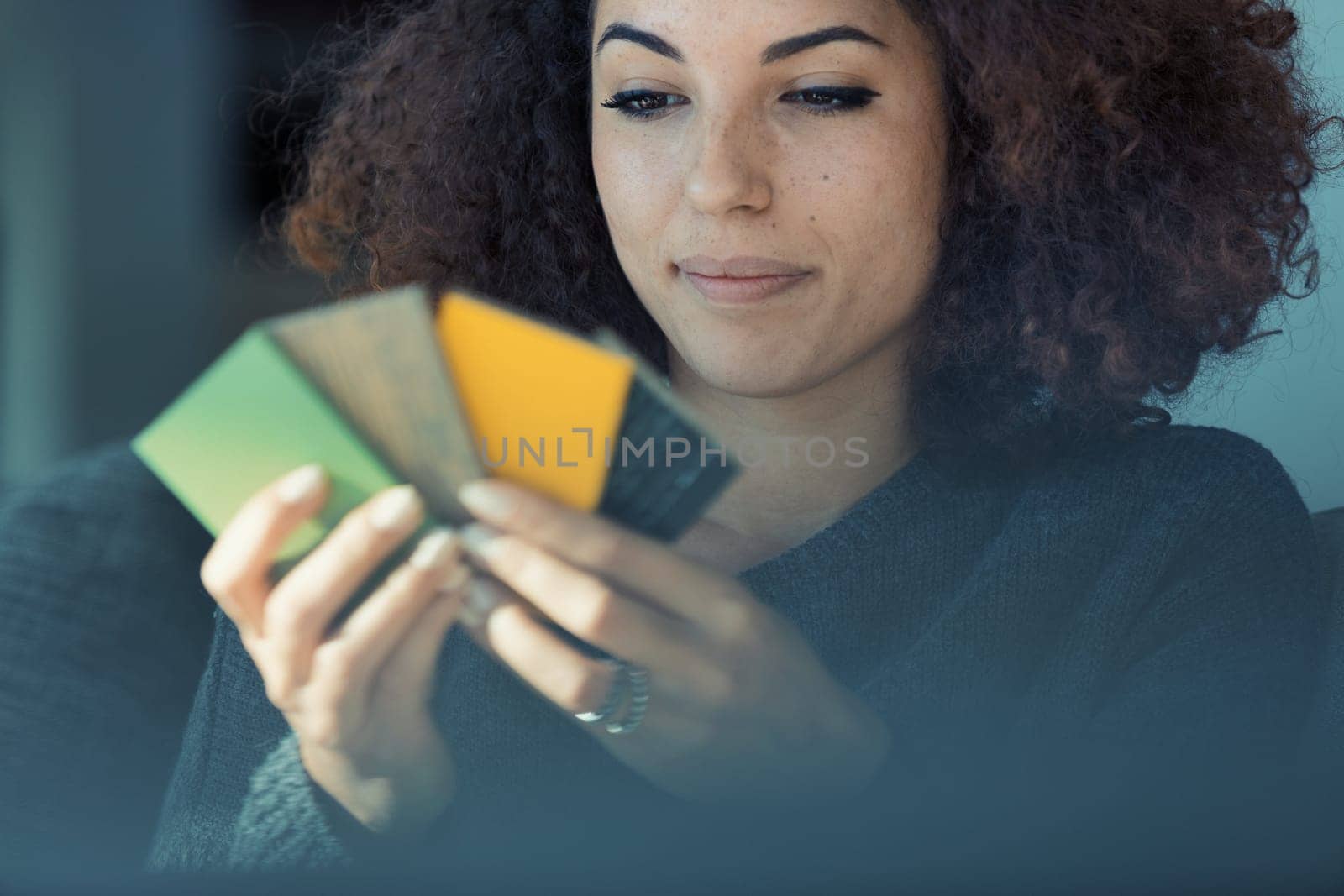 On her couch, a beautiful curly-haired woman with nice eyes browses color samples for furniture or floors. She enjoys and is deeply focused on tailoring her surroundings to match her lifestyle