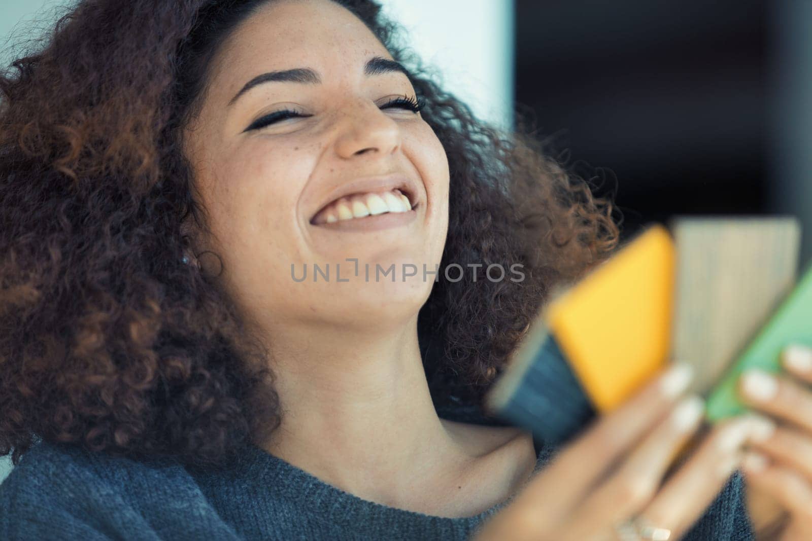 Curly-haired young woman chooses colors from a wood sample palette for her furniture or flooring, deeply engrossed and amused. Excited to personalize her lifestyle with her aesthetic taste, she's beau