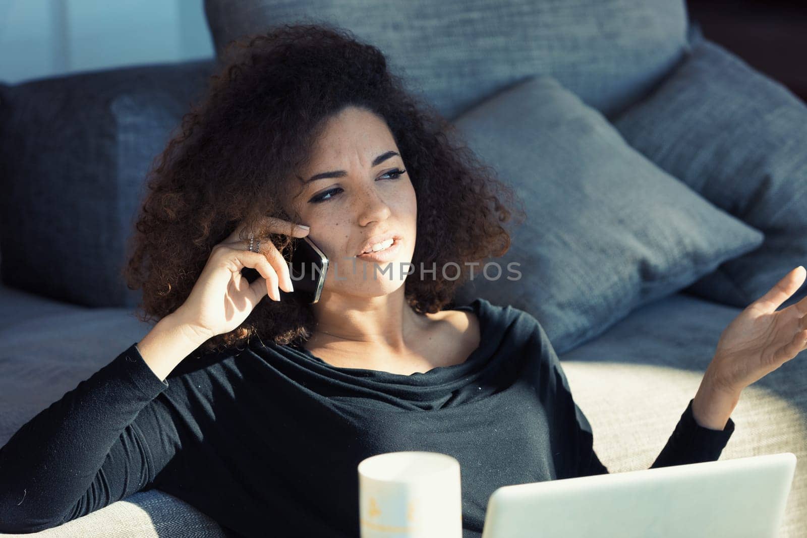 An ambitious young businesswoman conducts a phone call in her elegant setting. She's engaged in business discussions, devoting her full attention. With her curly hair, she exudes supportiveness and at