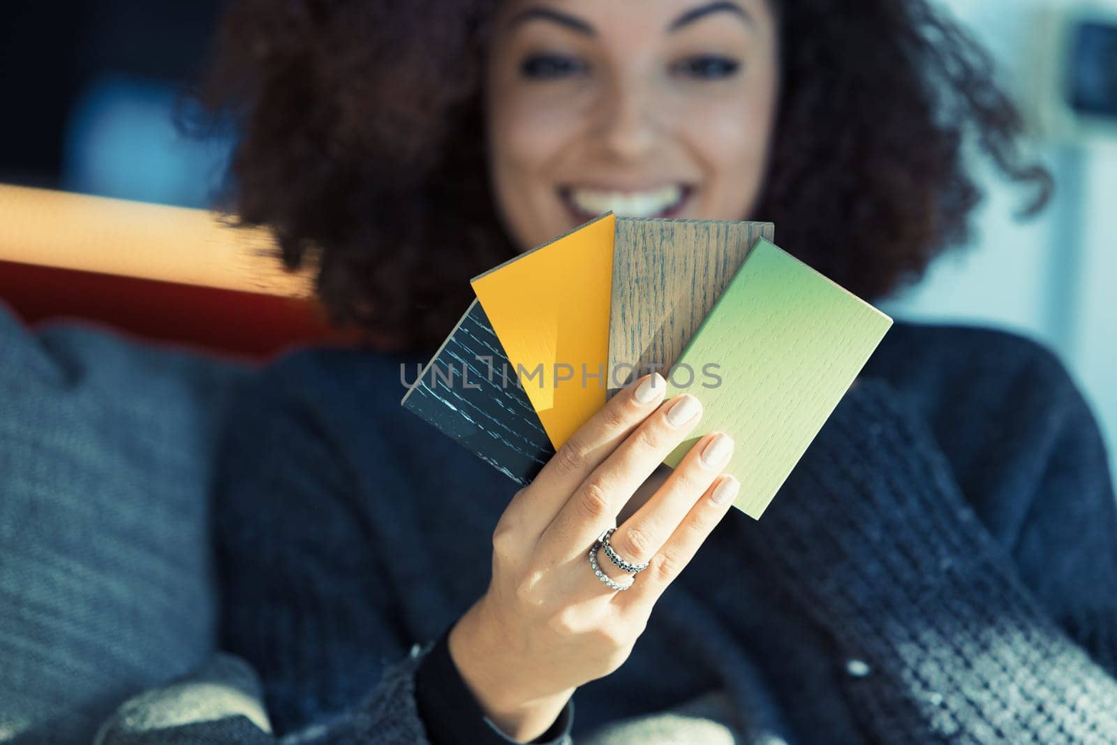 A beautiful ethnic-looking girl, engrossed in selecting colors from a sample chart on her couch, expresses her aesthetic style in designing her living space. She's radiant, with perfect teeth