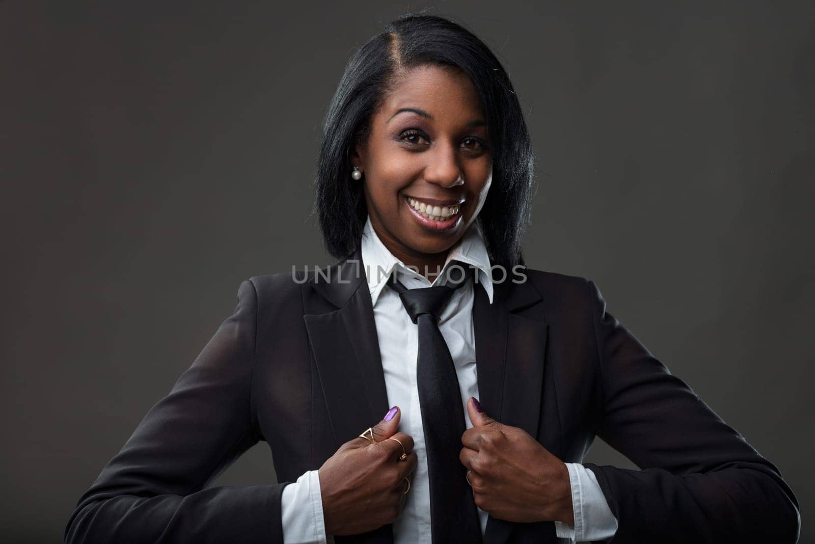 Black businesswoman with radiant smile adjusts her tie, exuding confidence and professional flair