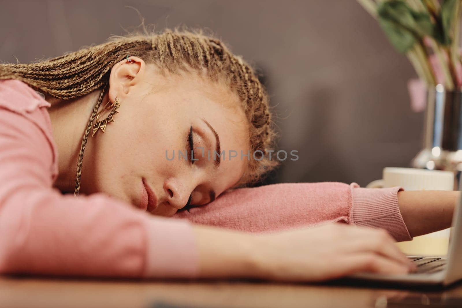 Young woman with box-braids falls asleep on laptop keyboard, hand on cellphone. Exhausted from work or study