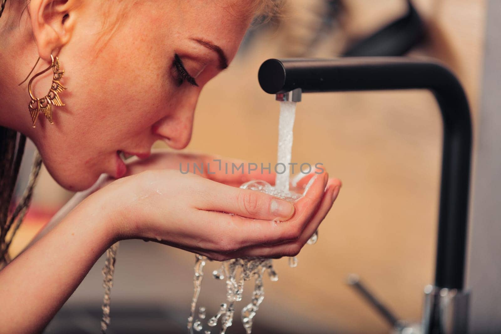 Young lady with gold earring, enjoying fresh tap water in kitchen. Symbolizes humanity's shared blessings