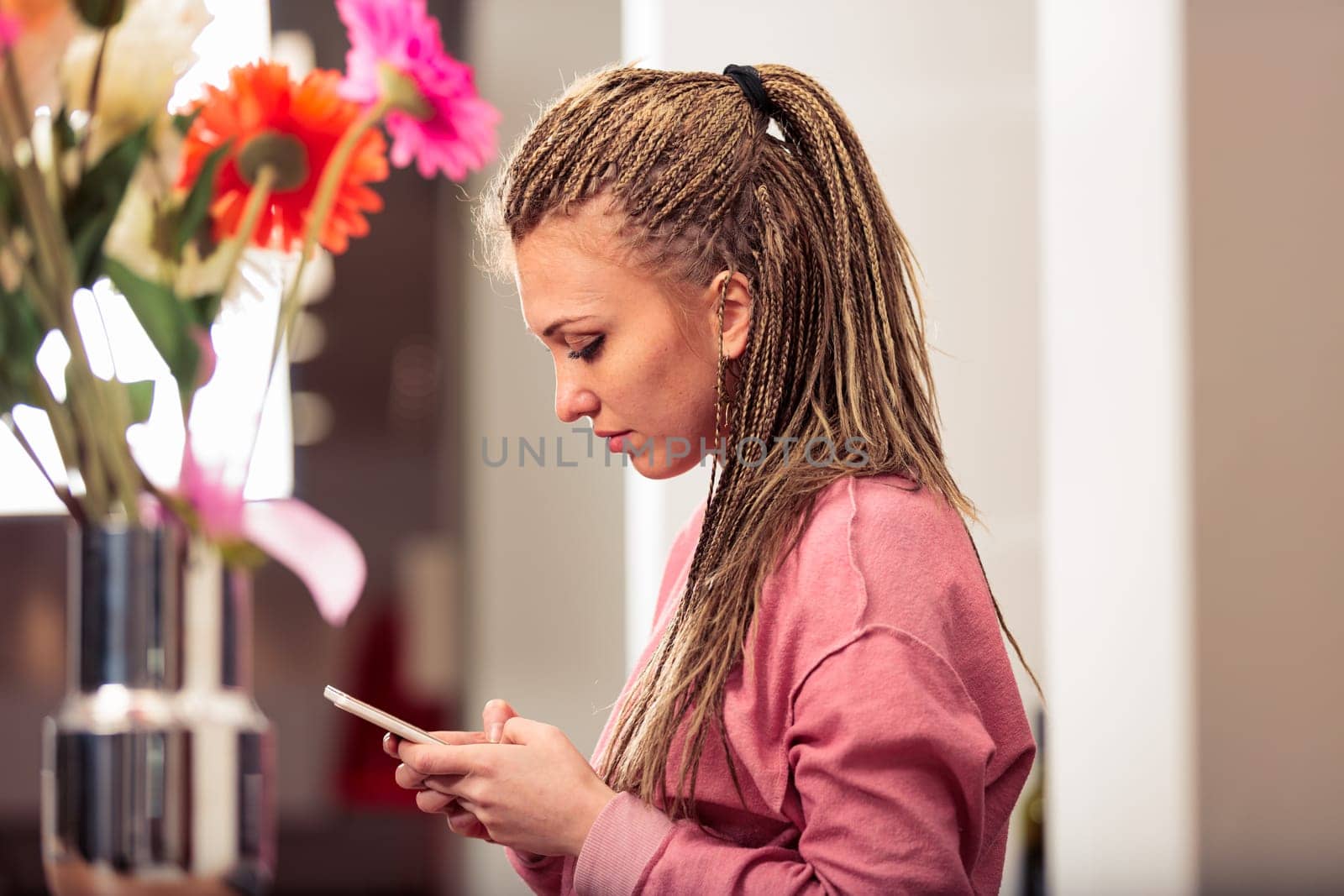 In her kitchen, a girl with box-braid braids in a pink sweatshirt engages with games and apps, modern entertainment