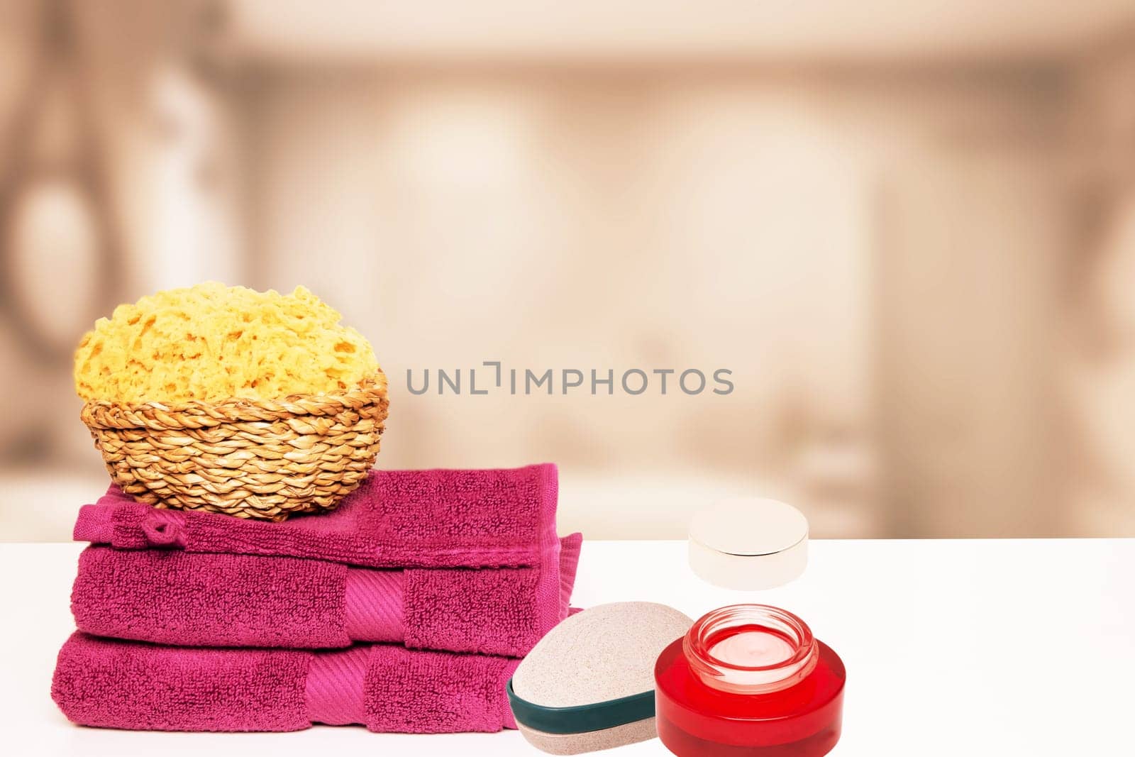 Closeup of fresh soft terry bath towels and soap, shampoo bottles and a basket with a natural sponge on table over blurred bathroom background. Copy space.