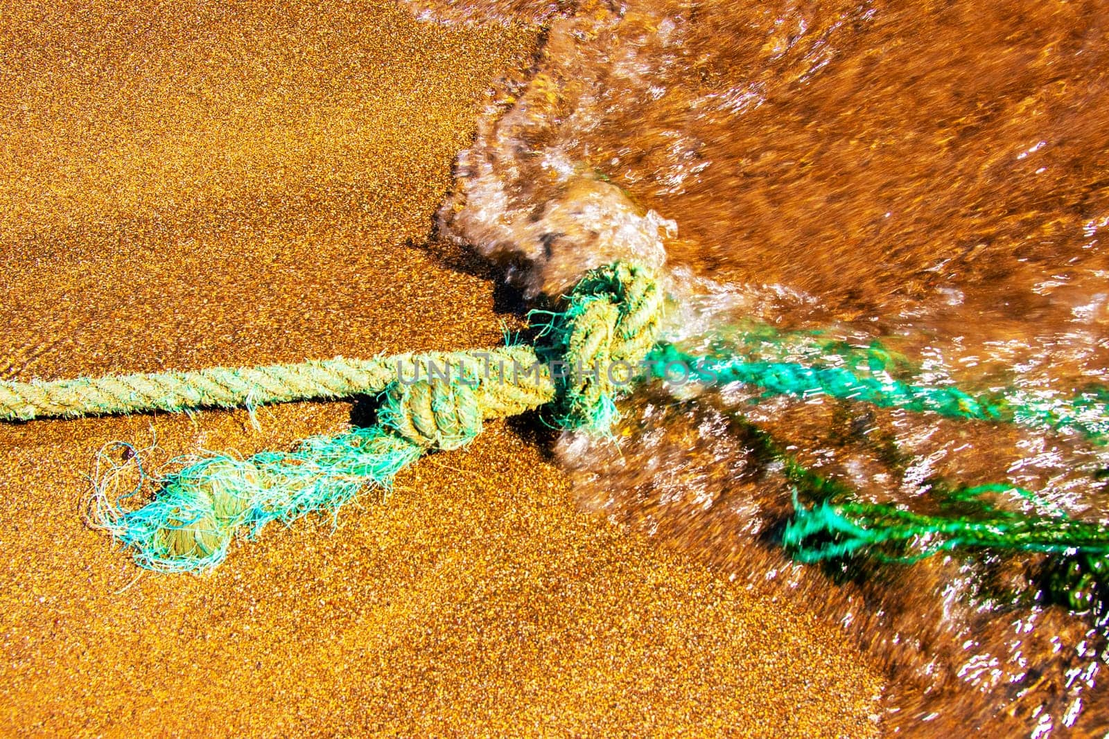 Closeup of an old nautical rope for mooring fishing boats on the Atlantic Ocean in Gran Canaria during an incoming water wave. Rope and knot background texture.