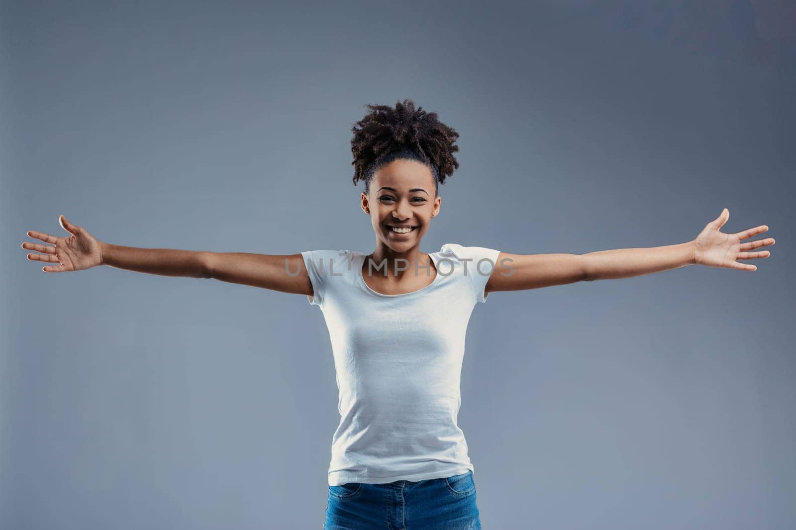 Open-armed young woman in white shirt beams with joy, offering a hug in a friendly manner