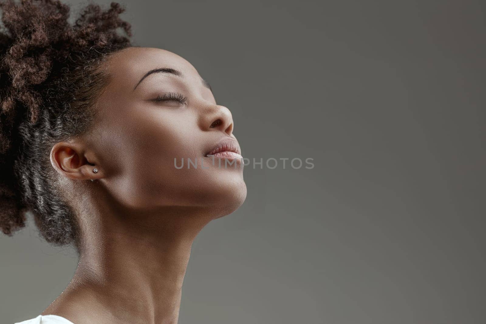 Serene young woman with eyes closed, head tilted upwards, exuding a sense of peaceful contemplation