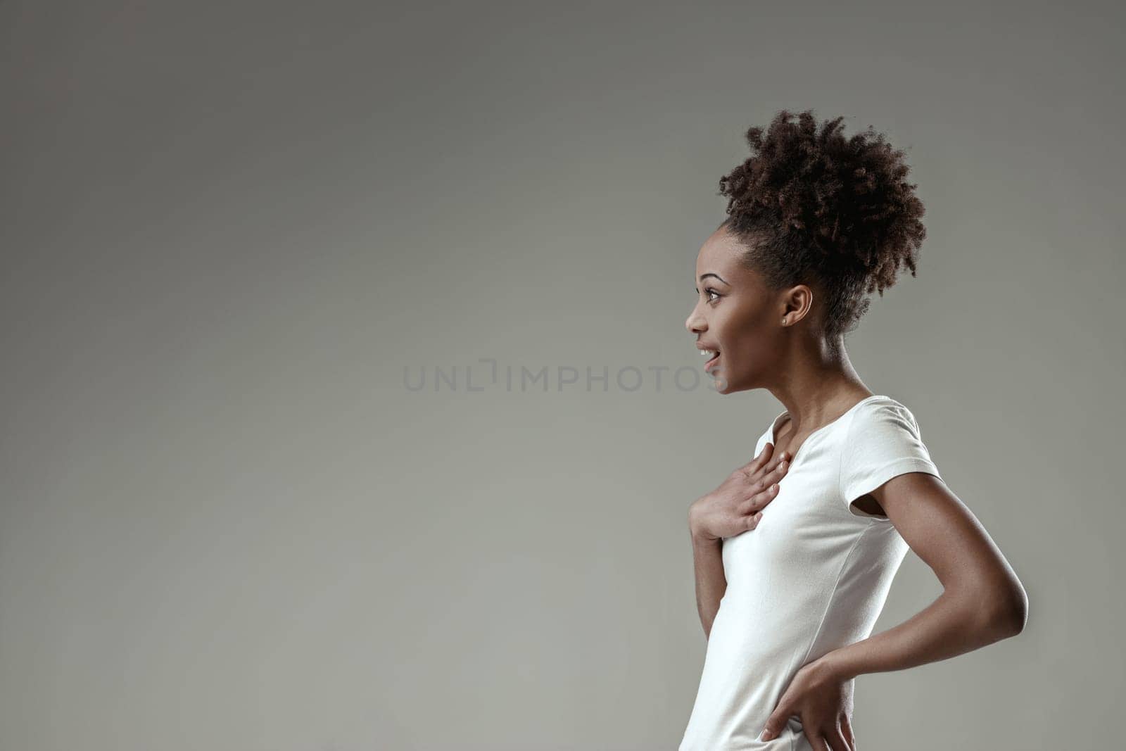 Surprised young woman in a white tee, her hand touching her collarbone, eyebrows raised in astonishment