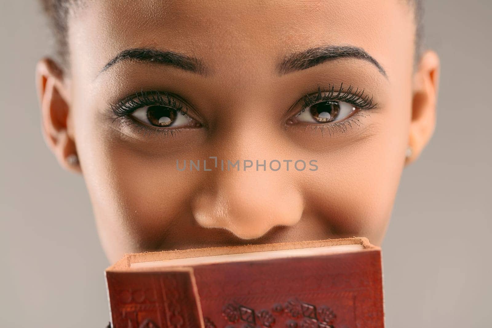 Young woman holding an ornate journal covers her face, leaving her intriguing eyes unveiled