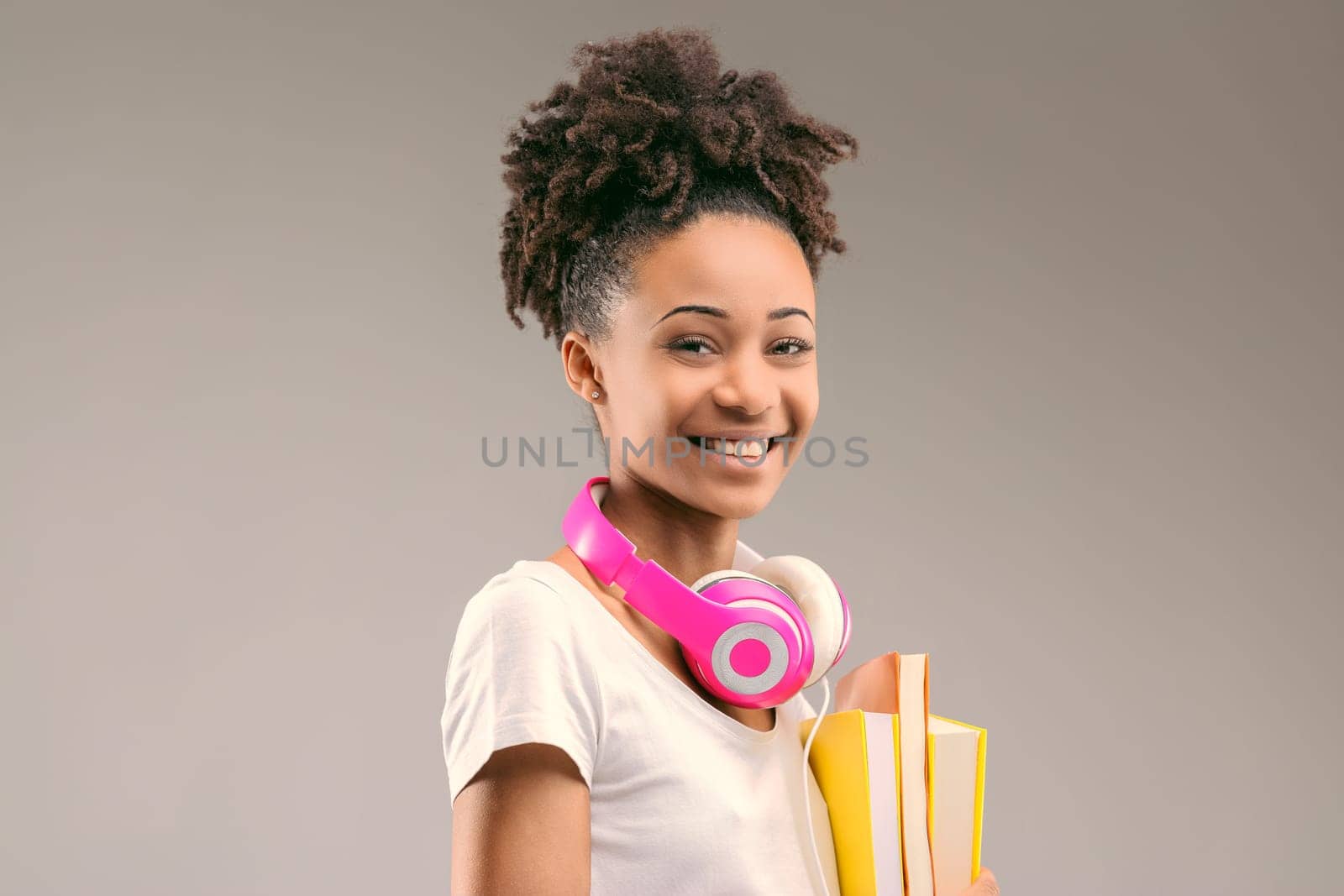 Eager learner sporting stylish headphones and an afro hairstyle, books in hand and smile wide